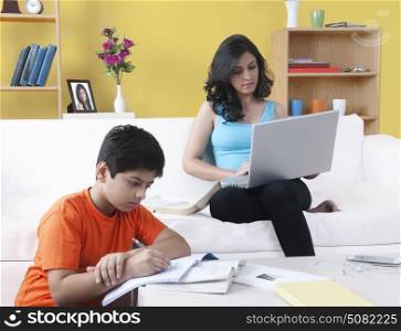 Brother doing homework while his sister using laptop