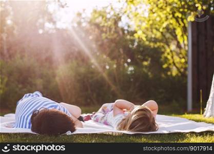 brother with his little sister outdoor back. two children lying on the grass in the garden