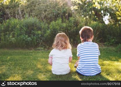 brother with his little sister outdoor back. two children sit on the grass in the garden