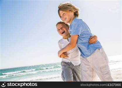 Brothers on beach hugging looking away smiling