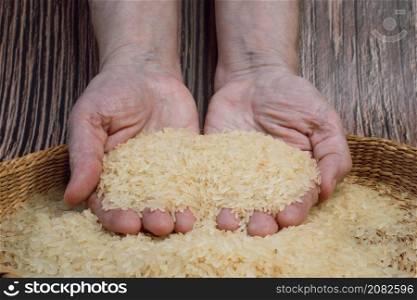 Brown bowl full of dry white rice grains. Hands full of fresh white rice grains. Healthy eating and vegetarian concept.