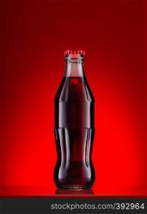 Brown carbonated drink in a bottle with a red cap on a red background. Brown carbonated drink in bottle with red cap