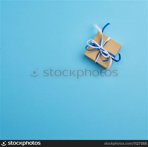 brown cardboard gift square box, bows on a blue background, top view. Festive concept, copy space