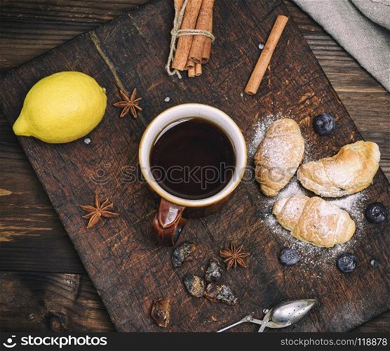 brown ceramic cup with black tea and croissants on a wooden board, top view. brown ceramic cup with black tea and croissants on a wooden boar