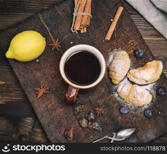 brown ceramic cup with black tea and croissants on a wooden board, top view. brown ceramic cup with black tea and croissants on a wooden boar