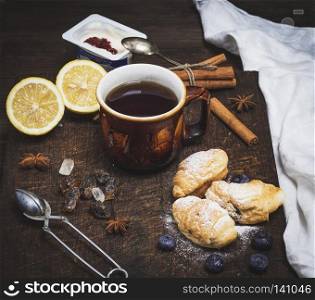 brown ceramic cup with black tea and croissants on a wooden board, vinatge toning