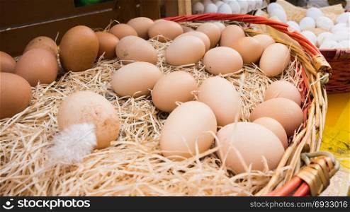 Brown chicken eggs leaning on straw in wooden basket at matket,outdoor.