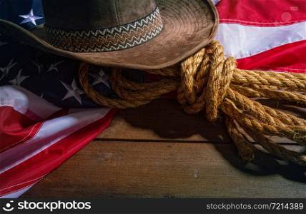 brown classic cowboy hat, coarse rope and big american flag lying on dark boards. Flag Rope Hat