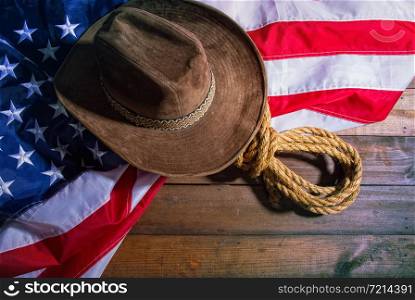 brown classic cowboy hat, coarse rope and big american flag lying on dark boards. Flag Rope Hat