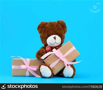 brown cute teddy bear and gifts wrapped in brown eco kraft paper and tied with a ribbon on a blue background, festive backdrop for Valentine&rsquo;s day, birthday