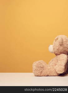 brown cute teddy bear sits sideways on yellow background, sadness