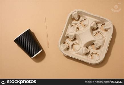 brown disposable corrugated cardboard cup, wooden stirring stick and holder on brown background. View from above