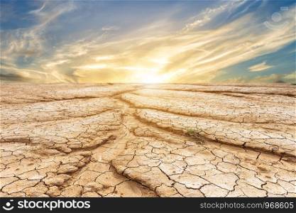 Brown dry soil or cracked ground texture on blue sky background with white clouds sunset.