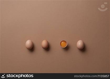 Brown eggs and one cracked egg with yolk on a brown paper background. Above view of three eggs and one half. Aligned organic eggs. Minimal image.