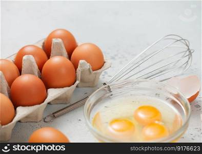Brown eggs in paper tray with yolk,whisk and shell on light kitchen table