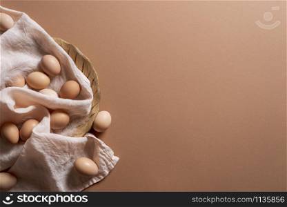 Brown eggs on linen towel and wooden plate on brown background. Above view of organic eggs. Minimal easter eggs. Chicken eggs freshly collected.
