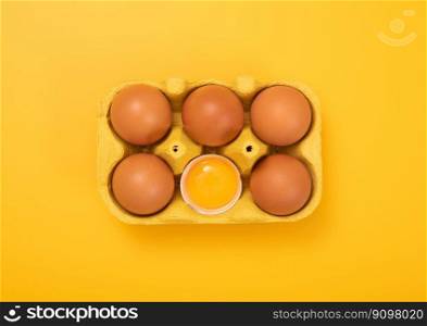 Brown eggs with yolk inside in paper tray on yellow background.Top view.