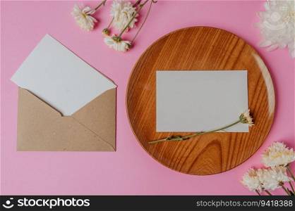brown envelope, flower and blank card on wood plate with pink background