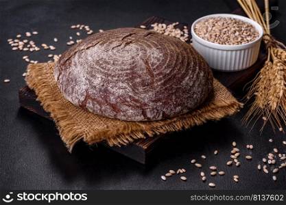 Brown fresh bread with seeds on a dark concrete background. Top view, copy space. Fresh baked homemade brown bread on a black concrete background with wheat grains
