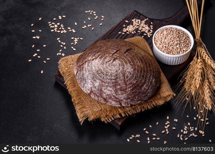 Brown fresh bread with seeds on a dark concrete background. Top view, copy space. Fresh baked homemade brown bread on a black concrete background with wheat grains