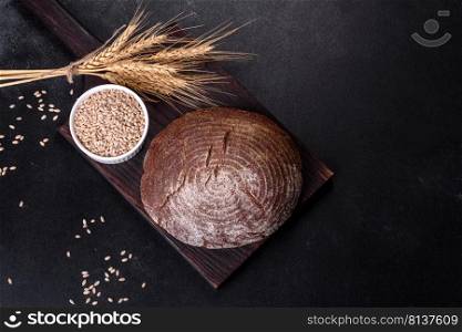 Brown fresh bread with seeds on a dark concrete background. Top view, copy space. Fresh baked homemade brown bread on a black concrete background with wheat grains