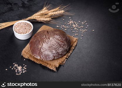 Brown fresh bread with seeds on a dark concrete background. Top view, copy space. Fresh baked homemade brown bread on a black concrete background with wheat grains