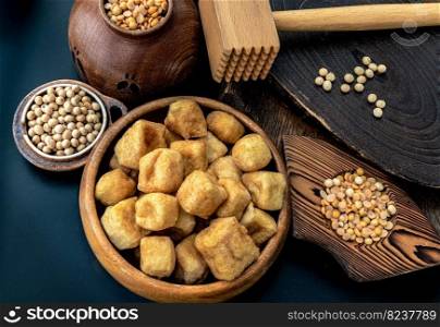 Brown fried tofu puffs or Deep Fried Tofu in wooden bowl and grains  soybeans  with dark background. Space for text.