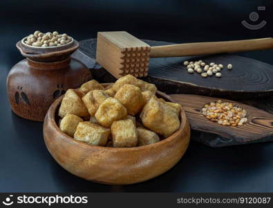 Brown fried tofu puffs or Deep Fried Tofu in wooden bowl and grains  soybeans  with dark background. Space for text.