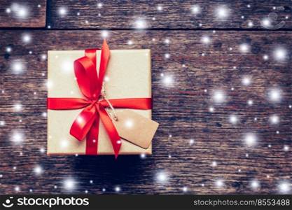 Brown Gift box and red Ribbon, Snow with tag on wood background with space.