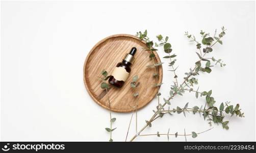 brown glass bottle with a pipette and an empty glued label on a wooden board, next to a branch of eucalyptus