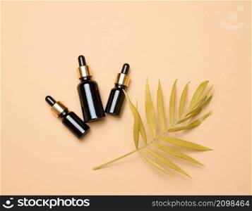 brown glass bottle with a pipette stands on a brown background. Container for cosmetics, serum and oil, palm leaf