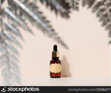 brown glass bottle with a pipette stands on a brown background. Container for cosmetics, serum and oil, silver fern leaf