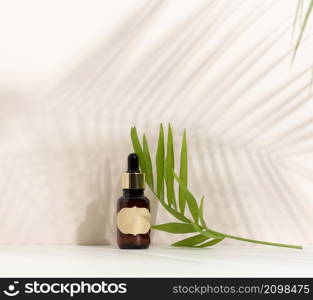 brown glass bottle with a pipette stands on a brown background. Container for cosmetics, serum and oil, palm leaf shadow