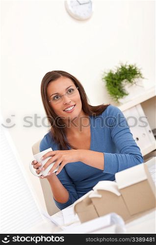 Brown hair female architect sitting at office holding cup of coffee