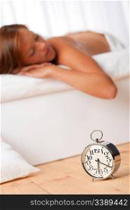 Brown hair woman lying in bed, alarm clock on wooden bed