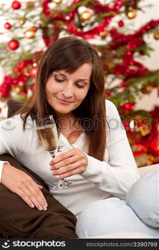 Brown hair woman sitting with glass of champagne on Christmas in front of tree