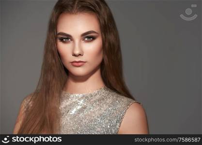 Brown-haired girl with long healthy and shiny Smooth hair. Care and beauty. Beautiful model woman in fashion dress on gray background