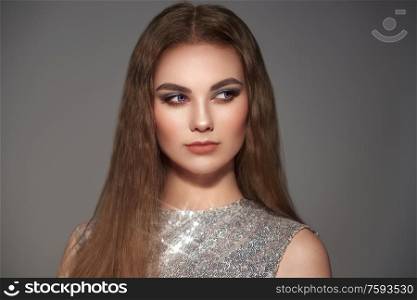 Brown-haired girl with long healthy and shiny Smooth hair. Care and beauty. Beautiful model woman in fashion dress on gray background