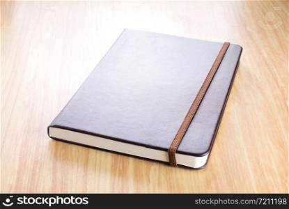Brown Hard cover notebook with elastic strap on wooden table in perspective view,Template for adding your title.