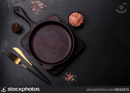 Brown iron empty pan with kitchen utensils on a dark concrete background. Cooking at home. Brown iron empty pan with kitchen utensils on a dark concrete background