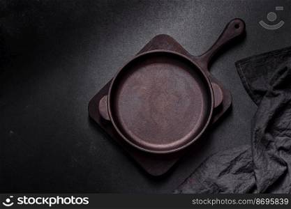 Brown iron empty pan with kitchen utensils on a dark concrete background. Cooking at home. Brown iron empty pan with kitchen utensils on a dark concrete background
