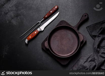 Brown iron empty pan with kitchen utensils on a dark concrete background. Cooking at home. Brown iron empty pan with kitchen utensils on a dark concrete background