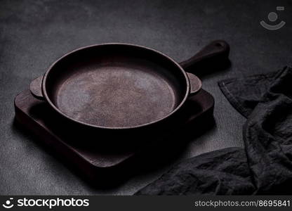 Brown iron empty pan with kitchen utensils on a dark concrete background. Cooking at home. Brown iron empty pan with kitchen utensils on a dark concrete background