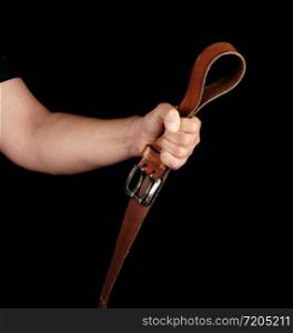 brown leather belt with an iron buckle in a man&rsquo;s hand, black background, concept of aggression