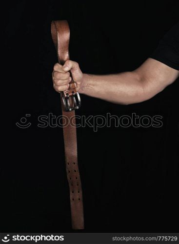 brown leather belt with an iron buckle in a man's hand, black background , concept of aggression and violence
