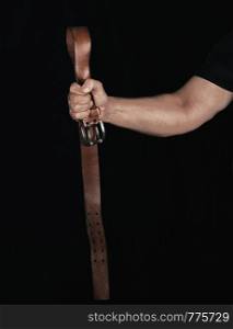 brown leather belt with an iron buckle in a man's hand, black background , concept of aggression and violence