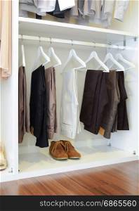 brown leather shoes and row of black pants hangs in wardrobe