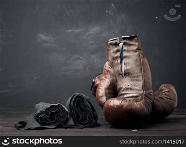 brown leather vintage boxing gloves and black elastic bandage for hands on a black background, sports equipment