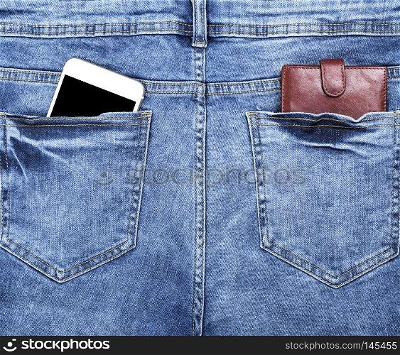brown leather wallet and a white smartphone with an empty black screen in the back pocket of blue jeans, close up