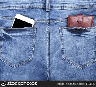 brown leather wallet and a white smartphone with an empty black screen in the back pocket of blue jeans, close up